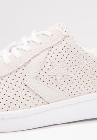 Beige mockalädersneakers med perforerad yta, texturerad finish, vit gummisula och kontrasterande sydda detaljer. Skosnören är vita.