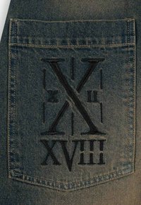 Niebieska kieszonka z denimu z czarnymi haftowanymi cyframi rzymskimi "X", "II", "XVIII", z widocznymi detalami szycia i teksturowanym materiałem.