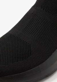 Černá teniska s prodyšnou pletenou strukturou. Disponuje bezešvým designem a silnou gumovou podrážkou pro odpružení a podporu.