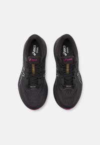 Baskets de sport noires avec une tige en mesh respirant, arborant des accents blancs, un logo violet et une semelle extérieure texturée.