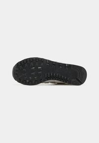 Semelle en caoutchouc noire d’une chaussure avec des rainures profondes et des motifs texturés, présentée sur un fond gris clair uni.