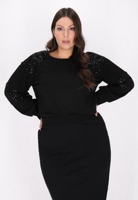 Sort sweatshirt med pailletpyntede ærmer. Lange ærmer, rund halsudskæring og en afslappet pasform, kombineret med en matchende sort nederdel.