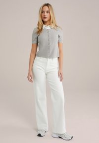 Harmaa lyhythihainen nappikauluspaita valkoisella kauluksella, yhdistettyinä leveälahkeisiin valkoisiin farkkuihin ja harmaisiin lenkkareihin. Yksinkertainen neulepinta ja istuva muotoilu.