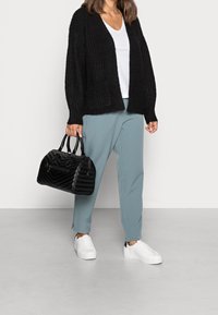 Cardigan lavorato a maglia nero su una t-shirt bianca, abbinato a pantaloni azzurri a sigaretta e sneakers bianche. Tiene una borsa a tracolla nera trapuntata.