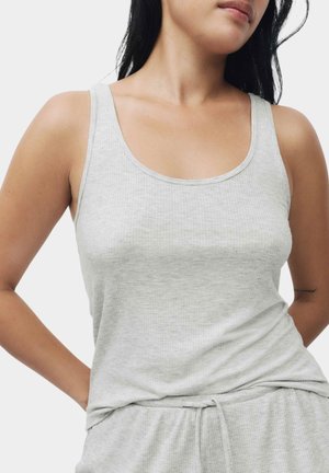 Kvinde iført en lysegrå ribbet tanktop og matchende bukser med snøre, stående med hænderne bag ryggen.