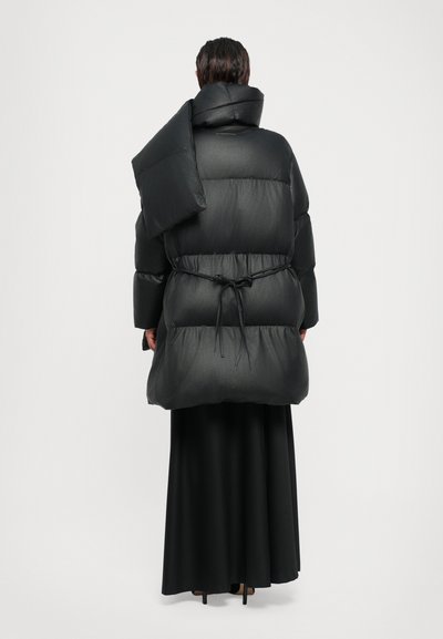 Μαύρο φουσκωτό μπουφάν με ψηλό γιακά, ραμμένο υφασμάτινο σχέδιο, oversized στυλ και ρυθμιζόμενη κορδόνι στη μέση. Διακοσμημένο με αποσπώμενο κομμάτι στον ώμο.