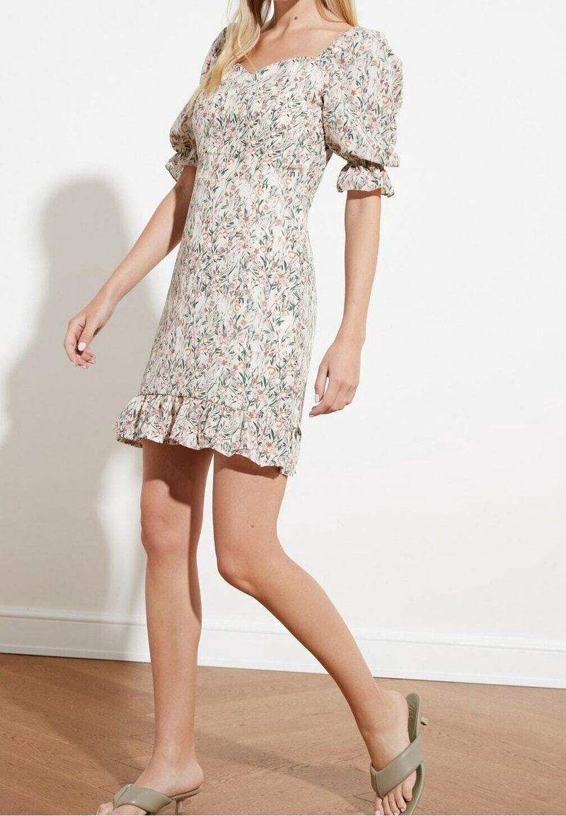 Robe florale avec manches bouffantes, décolleté carré et ourlet volé. Présente un fond clair avec de petits motifs roses et verts.