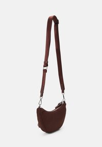 Bruine stoffen crossbodytas met een gebogen vorm, verstelbare band en zilveren hardware. Gladde textuur met een ritssluiting.