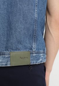 Jasnoniebieska kurtka dżinsowa o wyblakłej fakturze. Posiada zieloną skórzaną naszywkę w pasie z wytłoczonym logo "Pepe Jeans".