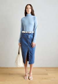 Hele sinine kõrge kaelusega särk, denim midi seelik ees oleva lõhiku ja valge vöödiga, kandes kreemikat käekotti ning jalas rihmadega valged sandaalid.