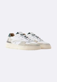 Een paar witte en beige low-top sneakers met groene accenten, suède details en geperforeerde neusdelen op een effen lichte achtergrond.