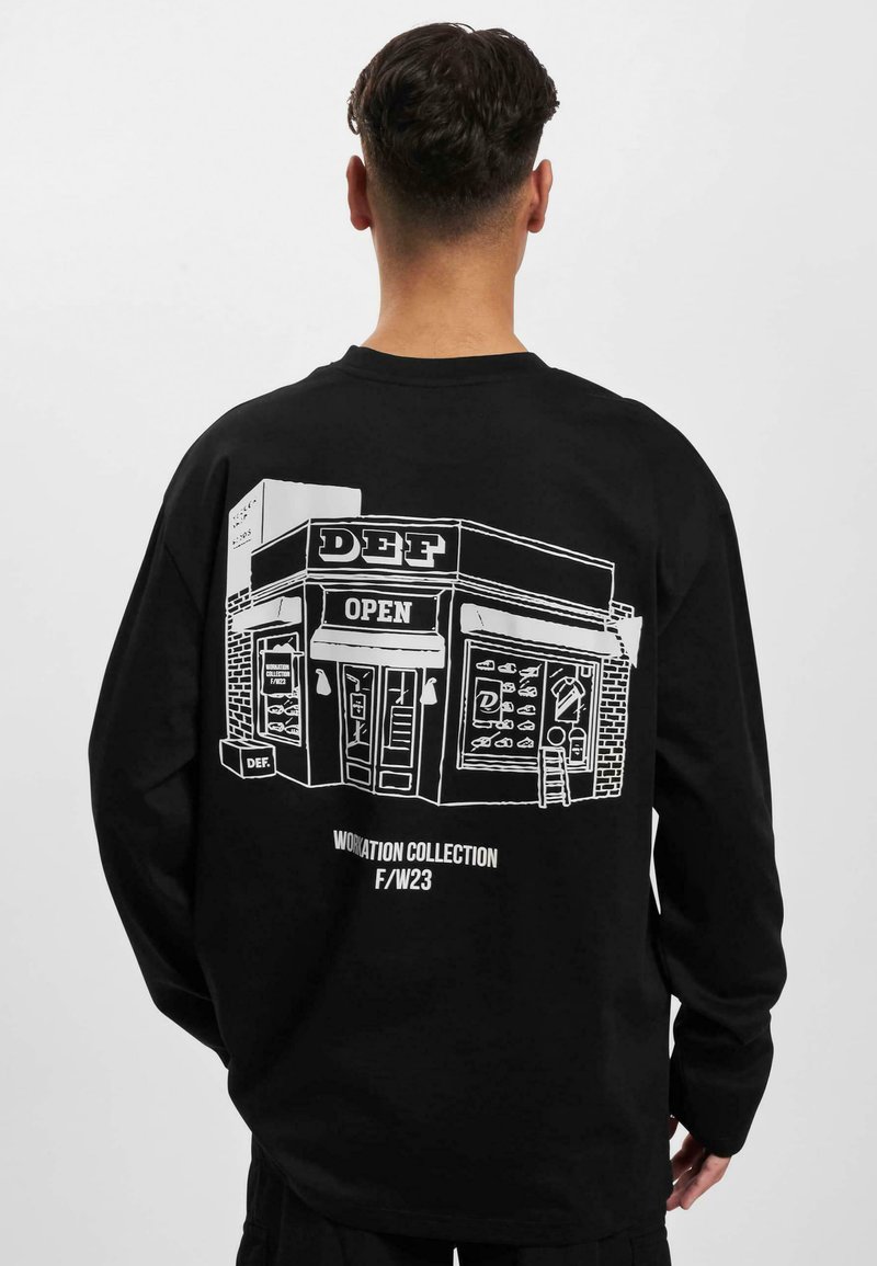 Sort langærmet sweatshirt med en hvid linjetegning af en butik, hvor teksten "DEF OPEN" og forskellige genstande i vinduet ses.