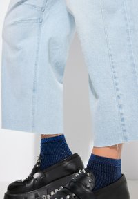 Ljusblå denimculotter med råa fållar, ihop med svarta kraftiga skor med silvernitar och blå ribbade strumpor med shimmer.