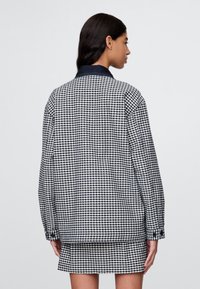 Ruuduline jakk tumesinise ja valge ginghami mustriga, klassikalise krae ja pikkade varrukatega, loodud mugavaks istuvuseks.