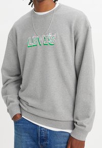 Felpa grigia con scollo rotondo, caratterizzata dal logo ricamato "LEVI'S" in verde e grigio. Realizzata in morbido tessuto misto cotone, vestibilità rilassata.