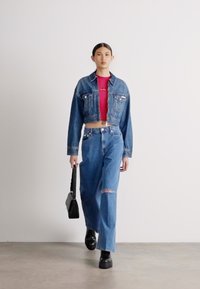 Jaqueta de ganga curta em lavagem média, blusa ajustada vermelha, jeans azuis de cintura alta com bainha desfiada e botas plataformas pretas. Bolsa preta.
