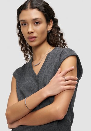 Gray knit top with a v-neckline, paired with silver jewelry: a sleek necklace, a bracelet, and a ring, highlighting smooth, polished surfaces.
