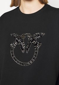 Felpa nera con un design circolare raffigurante due sagome di uccelli realizzate con strass neri e dettagli decorativi scintillanti.