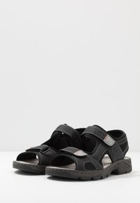 Svarta sandaler med justerbara remmar, öppen tådesign, texturerad syntetisk ovandel, meshdetaljer och vadderad innersula för komfort.