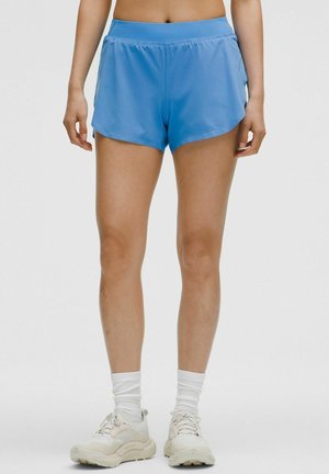 Ljusblå sportshorts med en lös passform, med hög midja och sidofickor för rörelse; kombinerat med vita skor och strumpor.