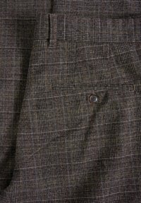 Närbild av bruna och grå rutiga byxor som visar en knappad bakficka och detaljer kring bältesöglor.