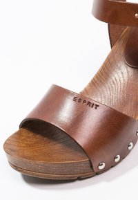 Sandale marron en cuir à bout ouvert avec semelle en bois, bride à la cheville, clous métalliques sur le côté et nom de la marque Esprit embossé sur la bride avant.