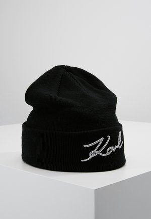 Czarna dzianinowa czapka typu beanie z podwiniętym mankietem i białym haftowanym, kursywnym logo „Karl” z przodu, prezentowana na białym podeście.