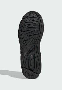 Black athletic shoe sole with textured rubber surface, featuring wavy tread patterns and circular accents for grip and flexibility.