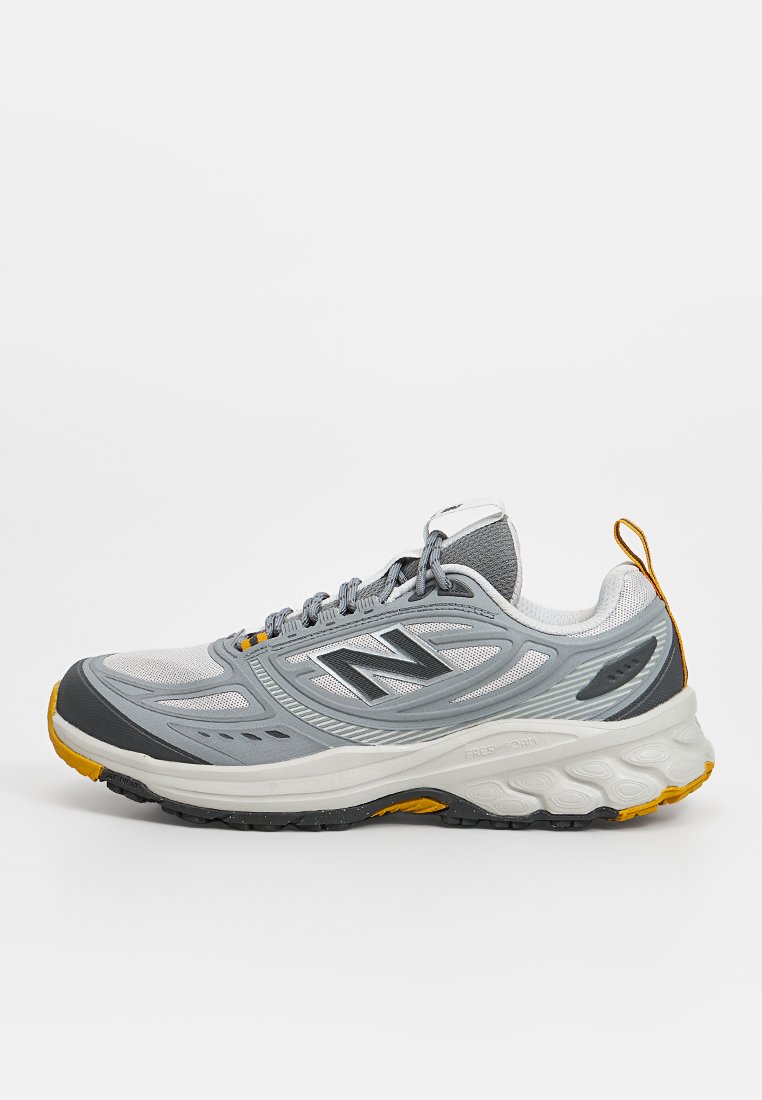 Zapatilla de running New Balance gris y blanca con detalles amarillos, parte superior de malla, suela acolchada y cierre de cordones mostrada en perfil lateral.