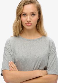 Grå kortærmet T-shirt med rund halsudskæring, blød tekstur og afslappet pasform. Modellens arme er korslagt, hvilket fremhæver skjortens snit.
