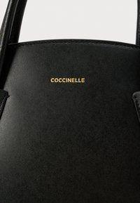 Borsa a tracolla in pelle nera con manici sottili e logo "COCCINELLE" dorato al centro del pannello frontale.