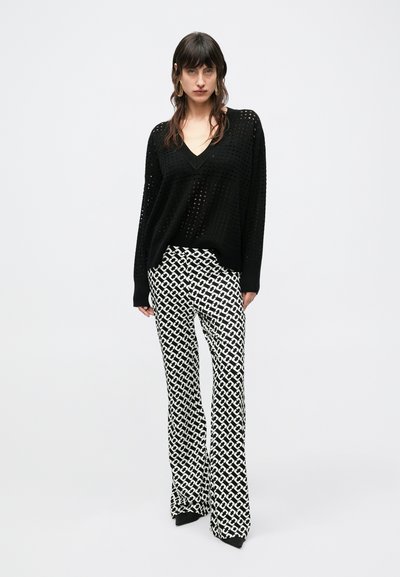 Mustast lõngast kootud V-kaelusega kampsun, millel on avatud koes muster; sellele on kombineeritud flööritud püksid, millel on mustvalge geomeetriline muster.