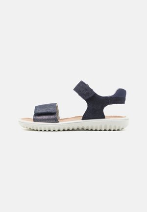 Navy blue sandal with a textured upper, adjustable strap, and white, ridged sole. Features a wide toe strap and a supportive ankle strap.