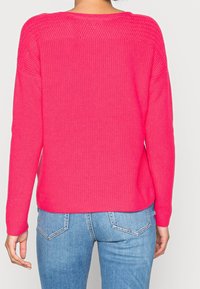 Felroze gebreide trui met een losse pasvorm, geribbelde boorden en een gestructureerd patroon aan de achterkant, gecombineerd met blauwe spijkerbroek.