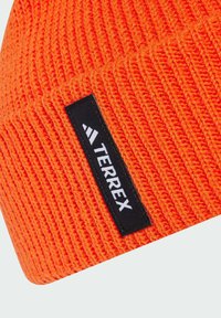 Berretto lavorato a maglia arancione con costine testurizzate, caratterizzato da un'etichetta rettangolare nera con il logo "TERREX". La vista ravvicinata mette in evidenza i dettagli del tessuto.
