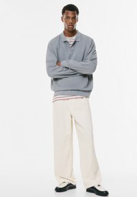 Lys grå oversized sweatshirt med et struktureret mønster, hvid og rød stribet skjorte under, beige brede bukser og sorte sko.