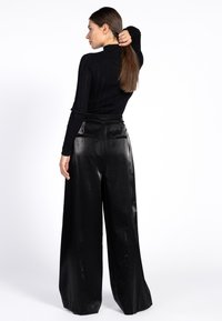 Zwarte geribbelde langemouwen top gecombineerd met hoge taille, wijde zwarte broek met een glanzende textuur en twee achterzakken.