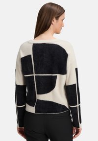 Gebreide trui in crème met zwarte abstracte geometrische patronen, met een relaxte pasvorm en een zachte, pluche textuur. Achteraanzicht weergegeven.