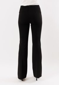 Pantaloni neri a zampa d'elefante realizzati in un tessuto morbido, vita media con zip sul retro e una vestibilità su misura che esalta la silhouette.