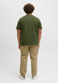 Olivegrønn bomulls t-skjorte med korte ermer, kombinert med beige bukser. Antrekket er komplettert med hvite sneakers. Enkel design, ingen mønstre.
