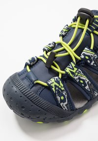 Námořnické sportovní sandály s texturovanou gumovou podrážkou, elastickými zelenými šňůrkami a vzorovanými látkovými popruhy. Mají zesílenou špičku a lehkou konstrukci.