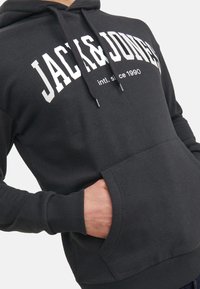 Schwarzer Hoodie mit weißem "JACK&JONES"-Logo, verstellbaren Zugbändern, Kängurutasche und gerippten Bündchen für eine bequeme Passform.