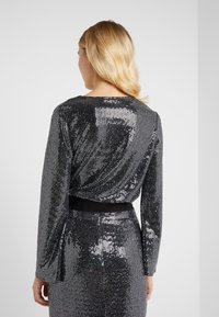 Abito con paillettes a maniche lunghe, tonalità nere e argento, collo rotondo, vita definita con una cintura nera. Superficie testurizzata riflettente.