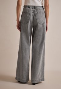 Jean large gris avec une texture usée, présentant une taille haute, de grandes poches arrière et un léger évasement au bas.
