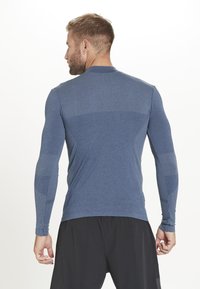Blå langærmet træningsskjorte med tekstureret øverste del; tætsiddende design. Har ribbede detaljer på skuldre og arme; letvægtsstof.