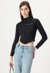 Čierna skrátená bunda s dlhými rukávmi, predným zipsom a malým logom "Juicy Couture"; kombinovaná s svetlomodrými džínmi s vysokým pásom.