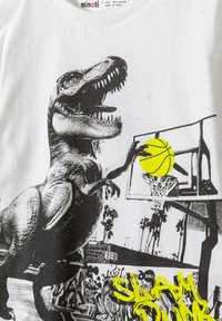 Hvid bomulds t-shirt med sort dinosaur grafik, der holder en basketball i hånden, gul bold accent og teksten "SLAM DUNK" i lys gul.