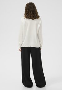 Biała bluzka z długim rękawem w połączeniu z luźnymi czarnymi spodniami o szerokich nogawkach. Gładki materiał o swobodnym kroju i delikatnej teksturze; minimalistyczny design.