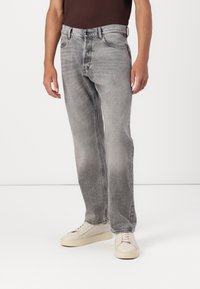 Jeans en denim gris avec un délavage clair, coupe droite, une fermeture à bouton, cinq poches et une décoloration subtile. Portés avec des baskets crème.