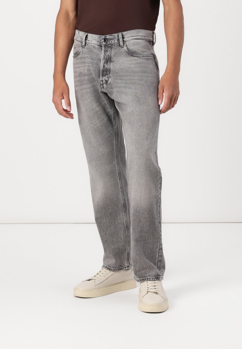Jeans en denim gris avec un délavage clair, coupe droite, une fermeture à bouton, cinq poches et une décoloration subtile. Portés avec des baskets crème.